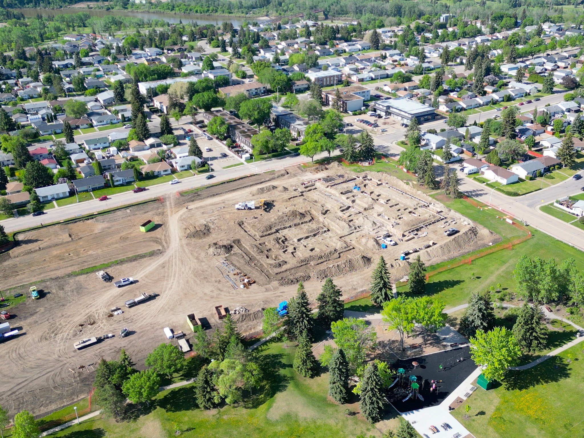 Aerial view of a construction site in a residential neighbourhood with visible foundations, equipment, and surrounding homes.